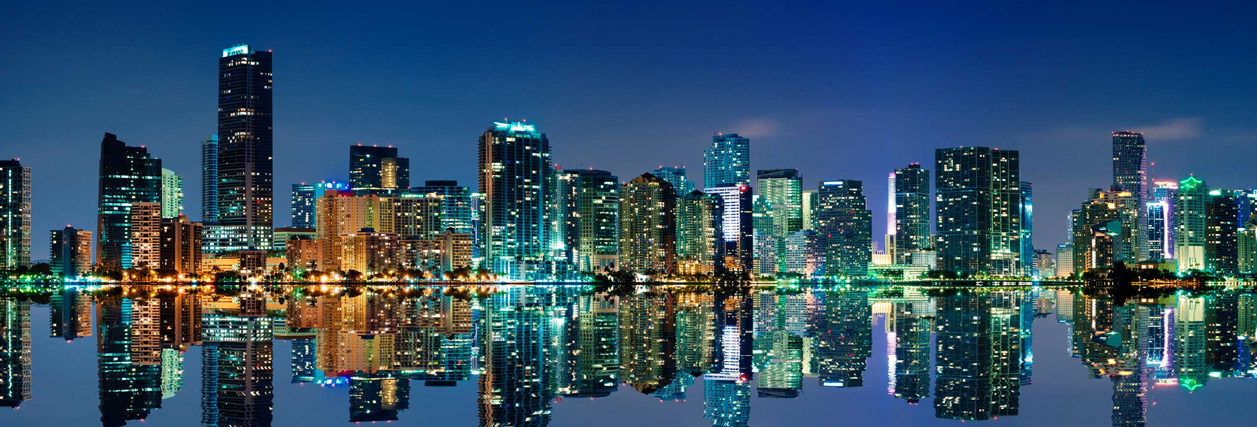 Miami city skyline at night with illuminated high-rise buildings reflected on water